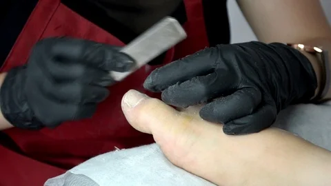 Pedicure master in red apron and black gloves works with nail file on girl toes Stock Footage 123012793