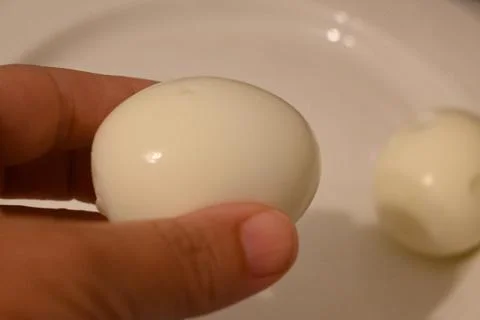 Peeled boiled egg held over a plate Stock Photos