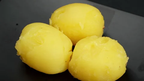 Peeled Boiled Yellow Potatoes Rotating on Black Plate Video stock 343970421