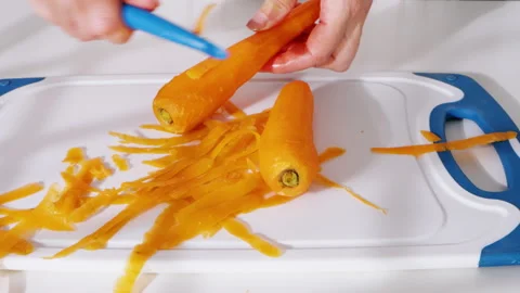Peeled carrots being held over a peeler and cutting board. Video stock 308154486