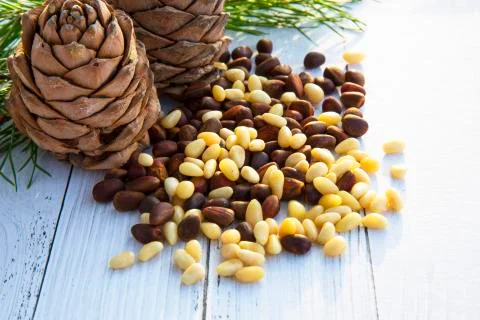 Peeled kernels of cedar nuts in a spoon, two pine cones, green branches Stock Photos
