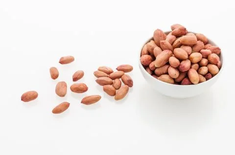 Peeled peanuts in a white ceramic cup and scattered grains on a Stock Photos