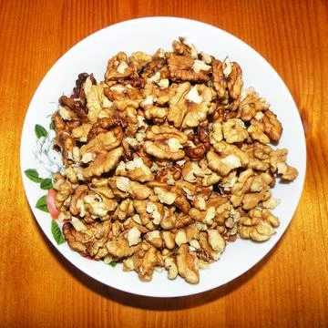 Peeled walnut kernels on a white plate over wooden background Stock Photos
