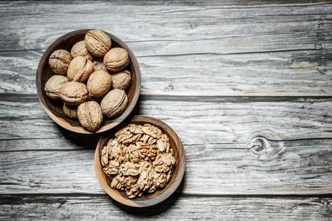 Peeled walnuts and nuts in a  shell in walnut wooden bowl on a wooden backg.. Stock Photos