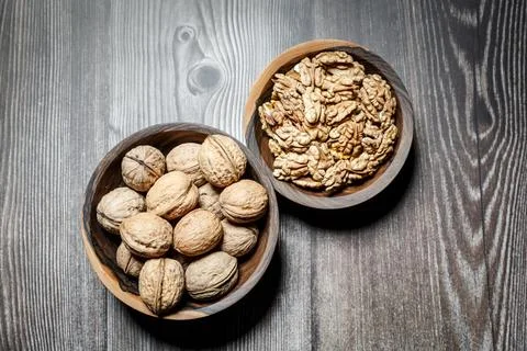 Peeled walnuts and nuts in a  shell in walnut wooden bowl on a wooden backg.. Stock Photos