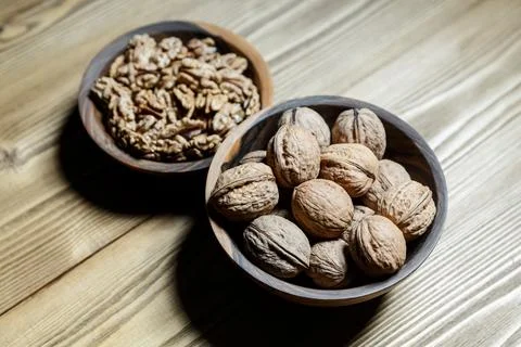 Peeled walnuts and nuts in a  shell in walnut wooden bowl on a wooden backg.. Stock Photos