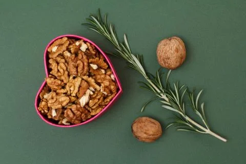 Peeled walnuts in gift box in shape of heart with unpeeled ones on green back Stock Photos