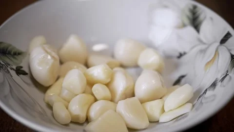 Peeled white garlic cloves falling into a floral bowl in slow motion Stock Footage 330118353