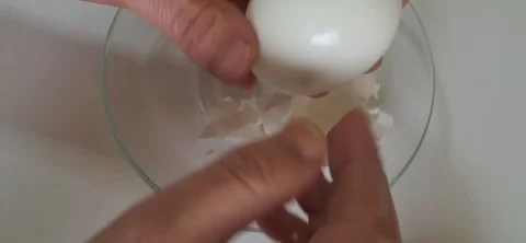 Peeling a boiled white egg over a glass bowl. 動画素材 334617880