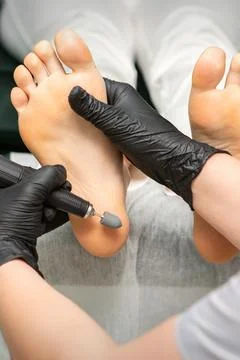 Peeling female feet. Hands of podiatry specialist in black gloves using special Stock Photos