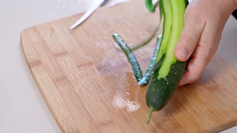 Peeling a fresh cucumber with a peeler over a bamboo board Stock Footage 346800211
