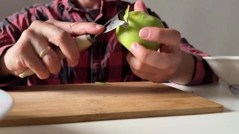 Peeling green apple with vegetable peeler on cutting board Stock Footage 337482480