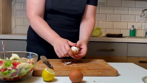 Peeling hard boiled egg by hand over wooden board in kitchen. salad ingredients Stock Footage 316472518