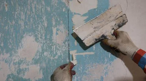 Peeling old wallpaper off a wall with a sharp spatula Stock Photos