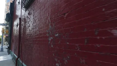 Peeling paint of an old red brick walled corner store bodega in New York Cit Stock Footage 242308995