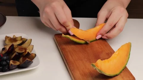 Peeling rind from orange melon and slicing into pieces on wooden cutting board. Stock Footage 316672767