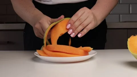 Peeling rind from orange melon slices by hand. Close-up of fruit preparation on Stock Footage 316675756