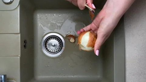 Peeling yellow onion over kitchen sink. Top view of hands using knife to clean Stock Footage 317106572