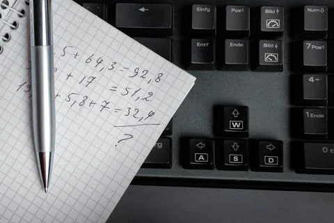 Pen and notes with arithmetic calculations on pc keyboard. Stock Photos