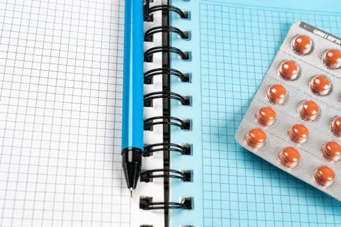 Pen and pills lying on a notepad for writing. Stock Photos