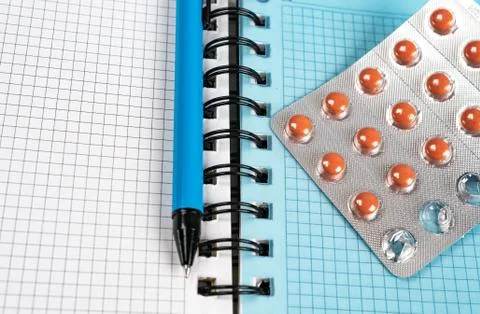 Pen and pills lying on a notepad for writing. Stock Photos