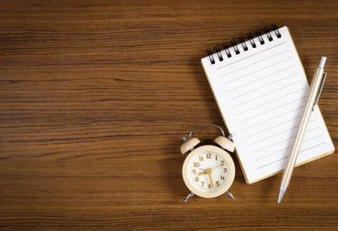 A pen on blank notebook and clock placed beside over wooden background. Stock Photos