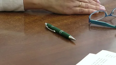 A pen lies on a brown table next to a woman's glasses Stock Footage 324766673