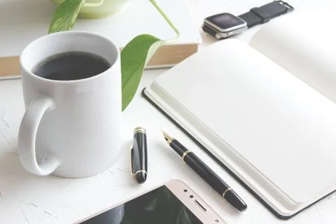 A pen on a paper notebook next a book and a mug with some coffee Stock Photos