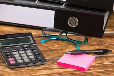 Pen on pink sticky note papers, calculator, glasses and black papers folder on a Stock Photos