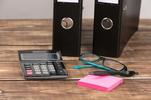 Pen on pink sticky note papers, calculator, glasses and black paper folders on a Stock Photos
