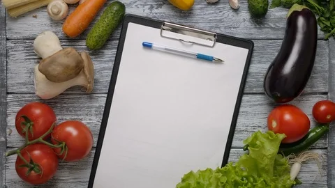 Pen rolling on blank clipboard on kitchen table with vegetables Stock Footage 121584863