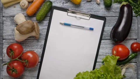 Pen rolling on clipboard on kitchen table with vegetables Stock Footage 119969891