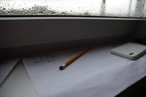 Pencil lying on scribbled paper on the windowsill on a rainy day. on the glas Stock Photos