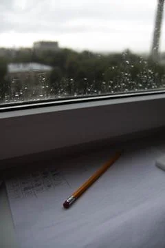 Pencil lying on scribbled paper on the windowsill on a rainy day. on the glas Foto stock