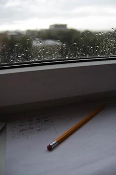Pencil lying on scribbled paper on the windowsill on a rainy day. on the glas Stock Photos