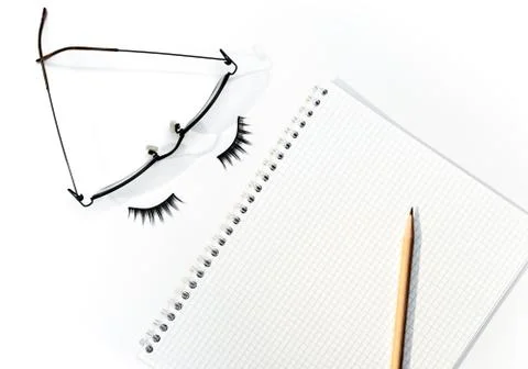 Pencil over open notepad with glasses and eyelashes. Stock Photos