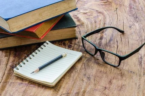 Pencil placed on a stack of books and notebooks with eyeglasses on a wooden f Stock Photos
