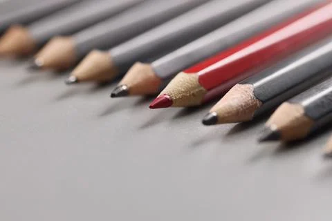 Pencils tips put on grey surface in strict order, red one among black pens Stock Photos