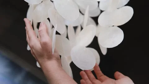 A pendant of white shells swings and rings in the wind. Wind music. Womens hands Stock-Footage 305864103