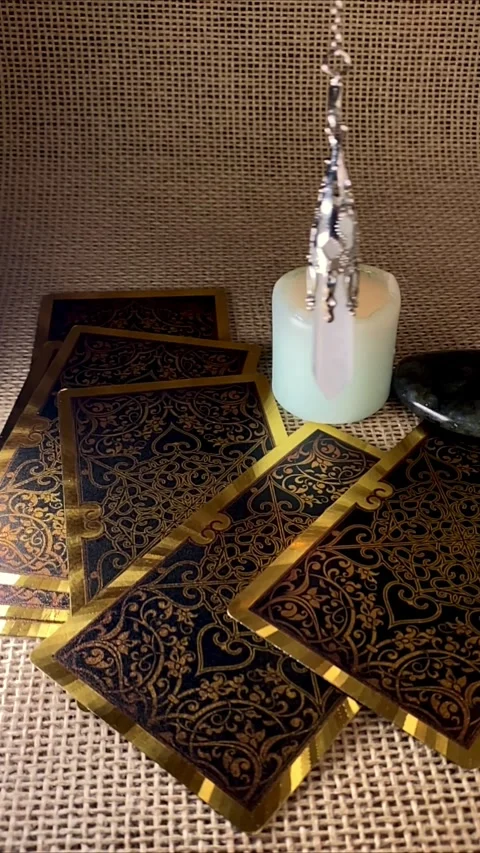 A pendulum swings gently over a burning candle and tarot cards Stock Footage 312823481