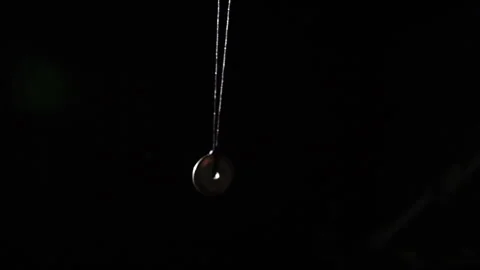 Pendulum used for hypnotism and readings swinging against black background Stock Footage 247173749