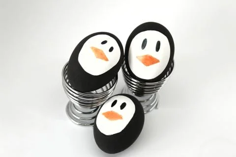 Penguin Easter Eggs on metal egg cup white background Stock Photos