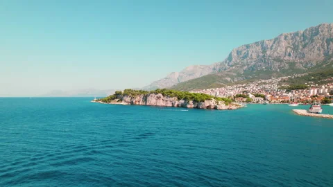 Peninsula edge with Cliffs rise beside calm sea waters. Makarska city merges Stock Footage 274556266