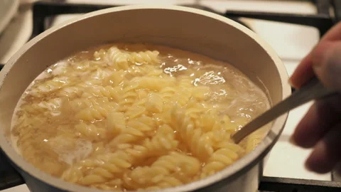 Penne pasta is cooked in boiling water, wooden spoon stirs pasta in slow motion Vidéo 127902072
