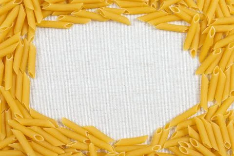 Penne pasta making a frame on rustic linen fabric Stock Photos