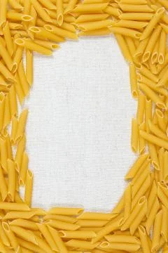 Penne pasta making a frame on rustic linen fabric Stock Photos
