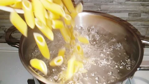 Penne rigate pasta splash falling into boiled water in the pot in a kitchen Stock Footage 95918198