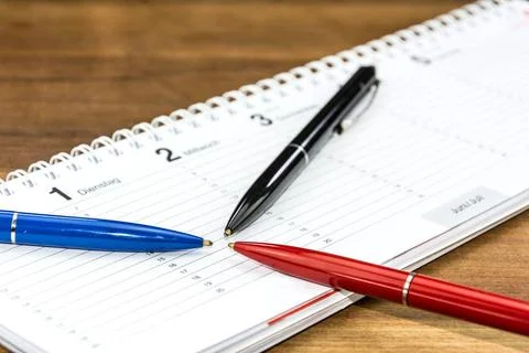 Pens lying on a schedule and pointing towards a specific date and time Pen... Stock Photos
