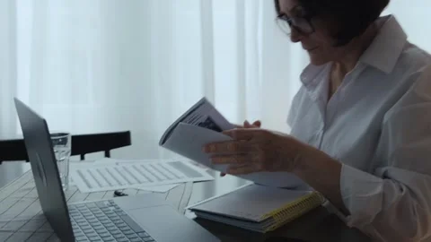 A pensioner sits in front of a computer and looking at documents. Stock Footage 242141347