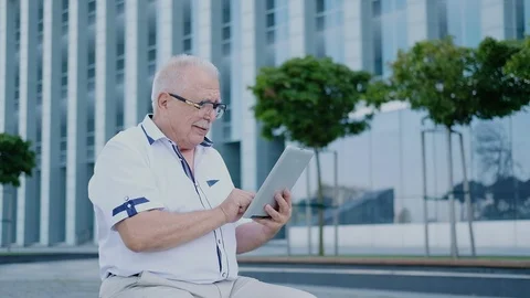 Pensioner uses tablet sitting on bench in city street Stock Footage 115884470